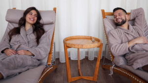 A happy couple wearing customized robes relax on spa chairs at a resort.
