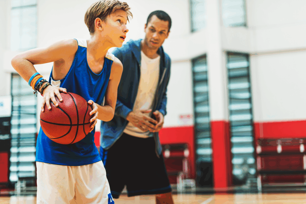 A student-athlete wears custom basketball apparel while practicing indoors with their coach.